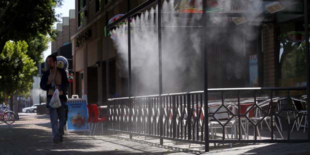 A pedestrian walks past an empty patio during lunch hour as misters spray in downtown Tempe, Ariz.,...