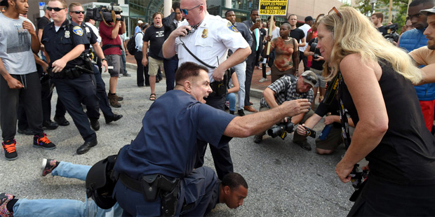 Baltimore Police try to control an angry protesters while detaining activist Kwame Rose as demonstr...