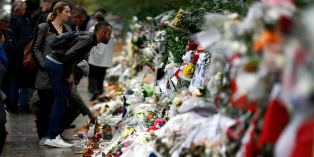 People look at flowers and card tributes placed outside the Bataclan concert hall in Paris, Thursda...