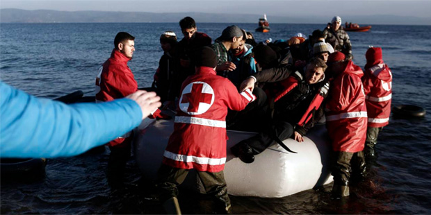Volunteers help refugees and migrants to disembark from a dinghy after their arrival from the Turki...