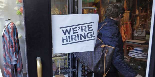 In this Wednesday, May 18, 2016, photo, a woman passes a "We're Hiring!" sign while entering a clot...