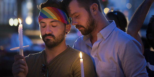 Eddie Desormeau, left, is consoled by Mike Post, right while holding candles during a moment of sil...