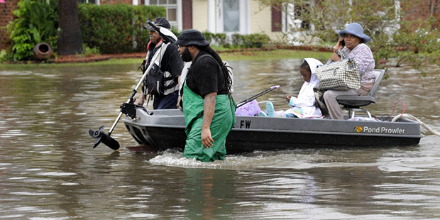 Volunteers pull a boat with a woman and young child as they evacuate from their homes Saturday, Aug...