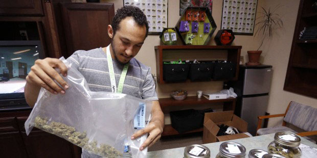 Budtender Miles Claybourne sorts strains of marijuana for sale into glass containers at The Station...