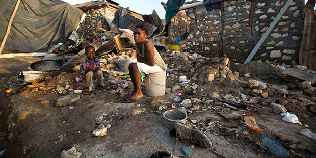A woman and a child sit on a buckets amid the ruins of their home destroyed by Hurricane Matthew, i...