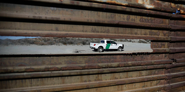 A Border Patrol vehicle drives by in Tecate, Calif., seen through a hole in the metal barrier that ...