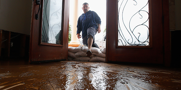 Nick Kriaris steps over sandbags as he enters his home onto mud-covered floors after his home flood...