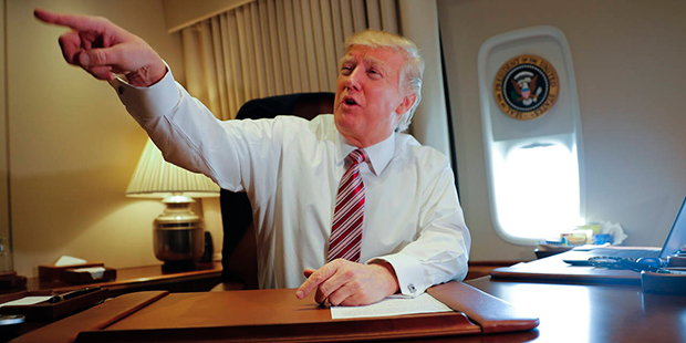 President Donald Trump points towards members of the media while seated at his desk on Air Force On...