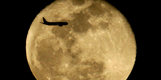 A passenger jet passes in front of the waning full moon as it approaches Sky Harbor International A...
