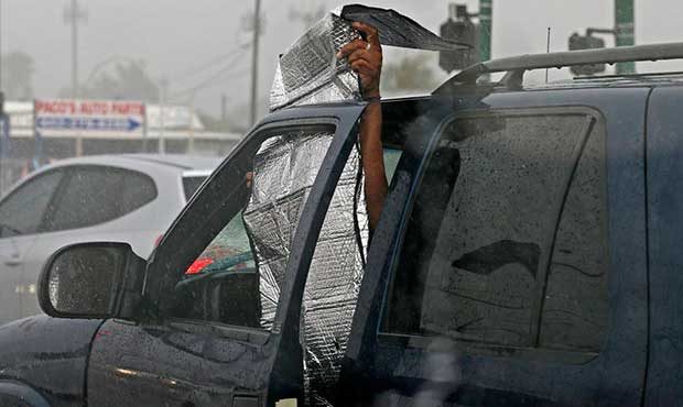 A driver attempts to block out the rain from a broken window as storms push through the Phoenix met...