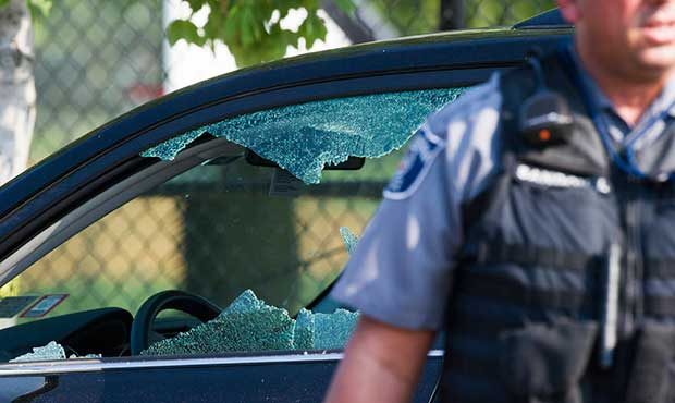 A police officer stands by an automobile with a damaged driver's window at the scene of a multiple ...