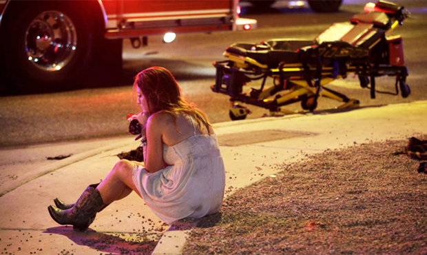 A woman sits on a curb at the scene of a shooting outside of a music festival along the Las Vegas S...
