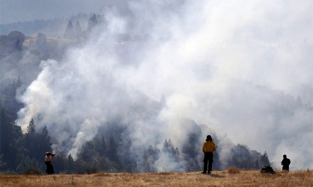 A firefighter, center, and two onlookers watch a smoldering wildfire from a hilltop, Sunday, Oct. 1...
