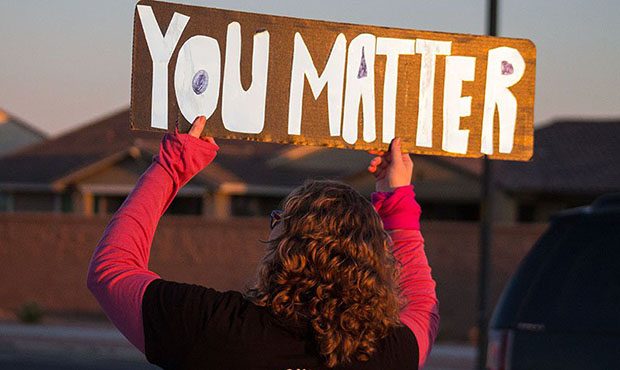 A member of Project Connect Four waves a sign for passing cars in front of Queen Creek High School....