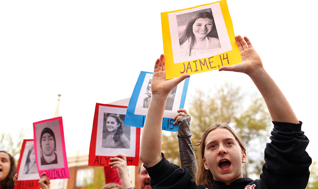Students form a wall and hold up the photos and age of victims of gun violence in front of the arch...