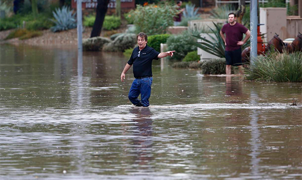 Pedestrians walk through a flooded street as they try to unclog storm drains during a flash flood a...