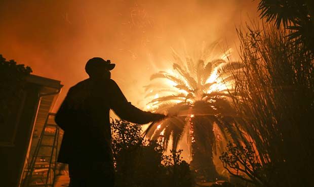 Park Billow, 27, sprays water on the hot spots in his backyard as the Woolsey Fire burns in Malibu,...