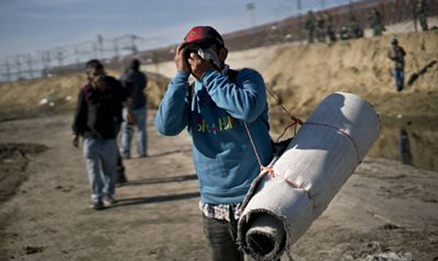 A migrant carrying a roll of carpet wipes his face after U.S. border agents fired tear gas at a gro...