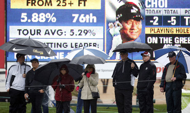 Fans, holding umbrellas, line up in front of the ninth hole during the second round of the Phoenix ...