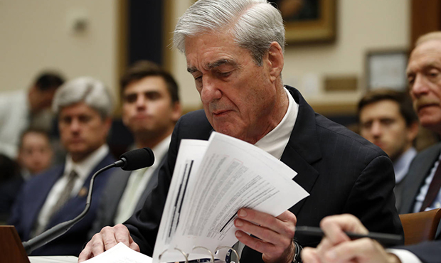 Former special counsel Robert Mueller checks pages in the report as he testifies before the House J...