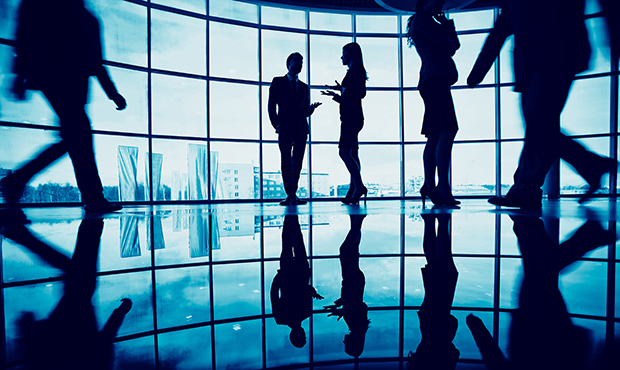 Several white collar workers communicating in office against window with two businessmen walking ar...