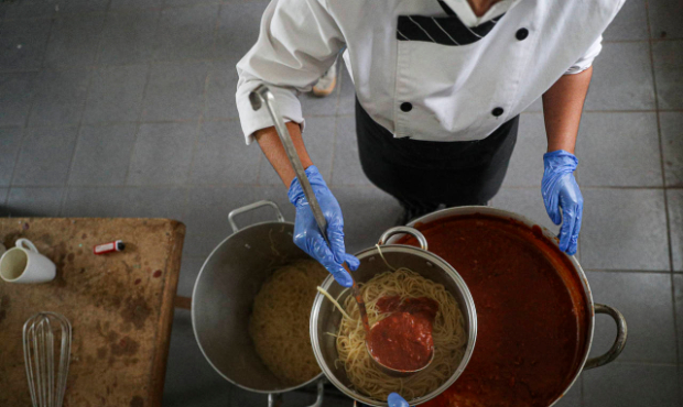 Chef Alejandra Albornoz ladles a red sauce over pasta as she and other volunteers prepare food to b...