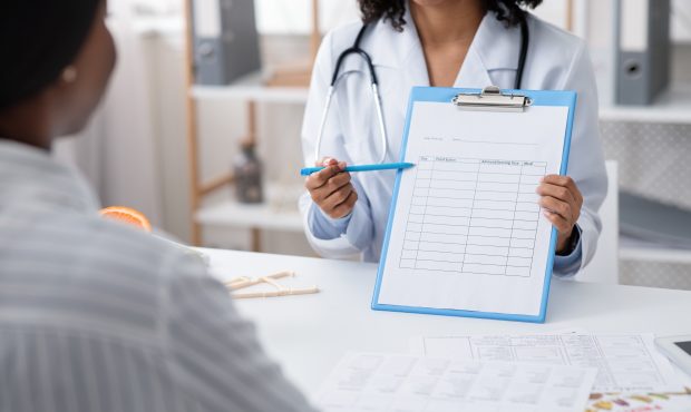 Black dietician showing female patient treatment plan, cropped, clinic interior...