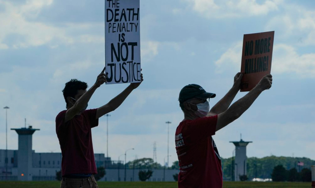 Death penalty protestors hold up signs across the street from the federal prison complex in Terre H...