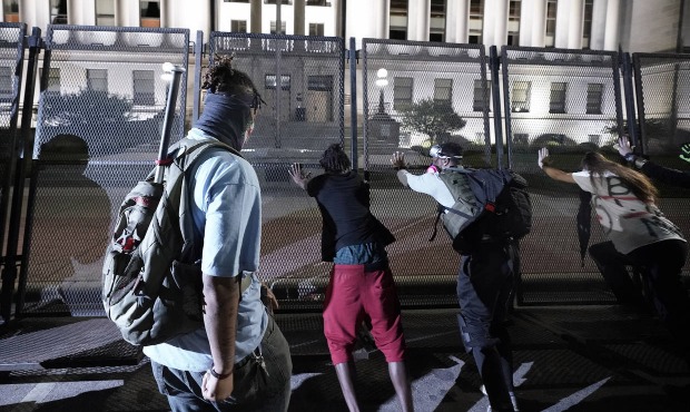 People try to push over protective fencing Tuesday, Aug. 25, 2020 in Kenosha, Wis. Anger over the S...