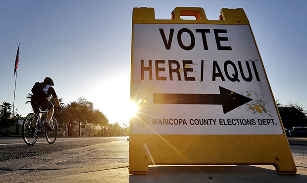 A cyclist rides past a sign directing voters to a primary election voting station early Tuesday, Au...