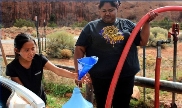 Zhane Atene, right, and her younger sister, Leighan, fill plastic containers with water to hauk bac...