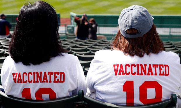 Fans wearing "Vaccinated" shirts sit the stands on Opening Day between the Boston Red Sox and the B...