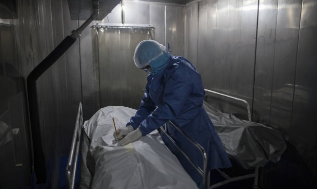 A healthcare worker fills out paper work for a patient who died from COVID-19, in a morgue at the S...
