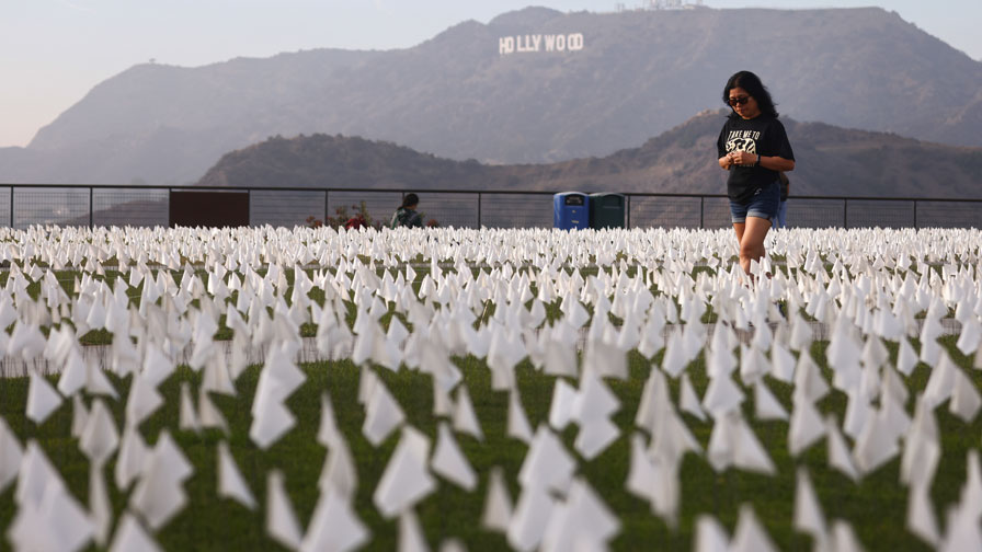 A person walks past a white flag memorial installation honoring the nearly 27,000 Los Angeles Count...