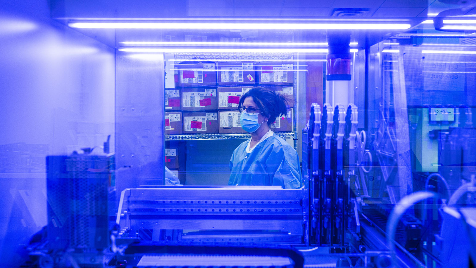 A medical technologist is seen through the window of a PCR analysis machine in the testing lab at Q...