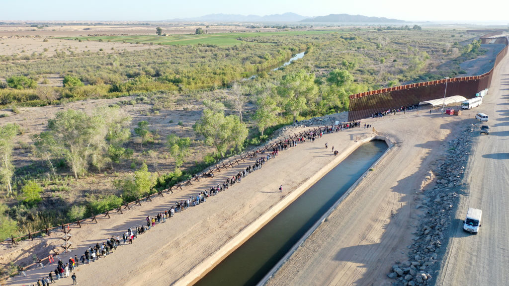 In an aerial view, immigrants seeking asylum in the United States wait in line near the border fenc...
