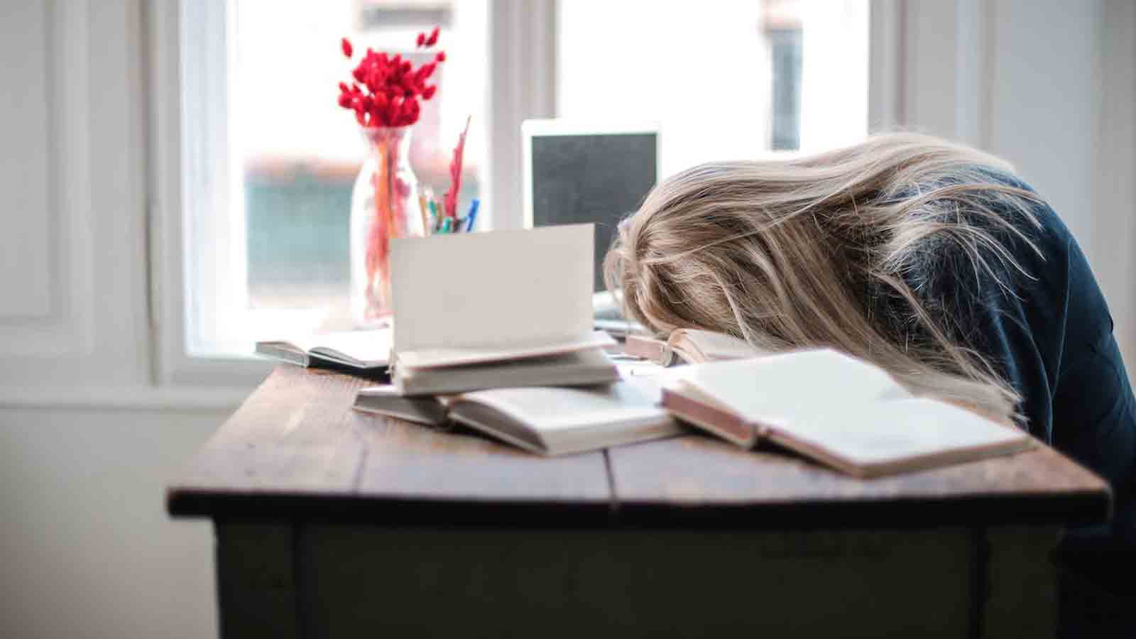 woman with her head resting on what appears to be textbooks at a table...