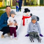 A mom and two kids pose with a snowman on a snowy field