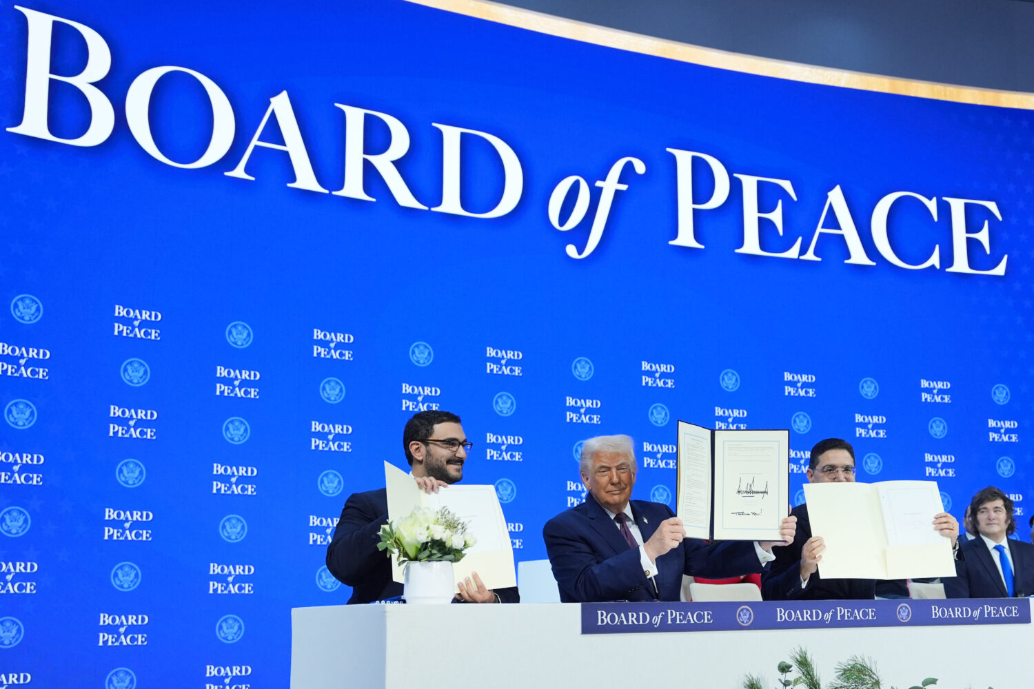 President Donald Trump, center, holds up a signed Board of Peace charter during the Annual Meeting ...