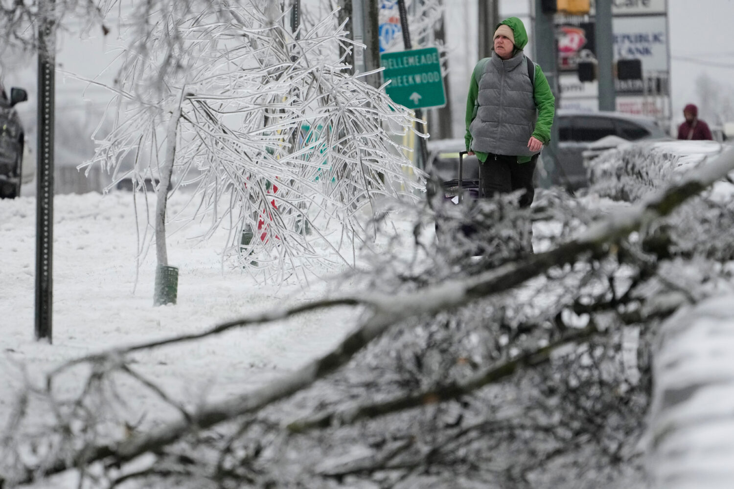 A person walks past ice covered trees and a fallen limb during a winter storm Sunday, Jan. 25, 2026...