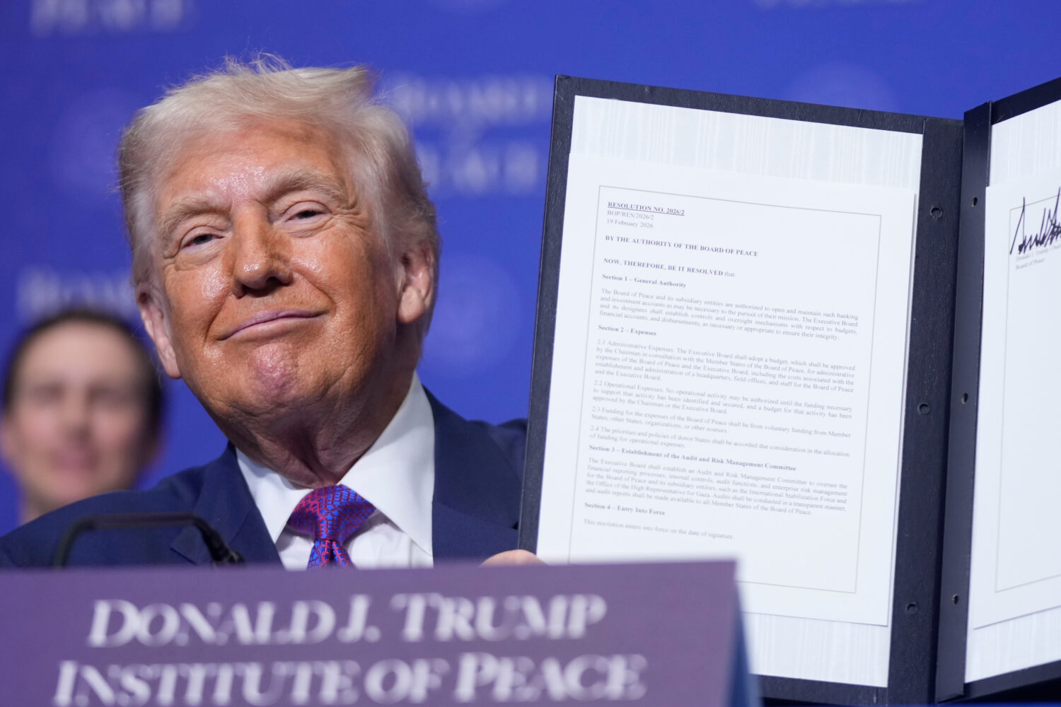 President Donald Trump holds up a signed resolution during a Board of Peace meeting at the U.S. Ins...