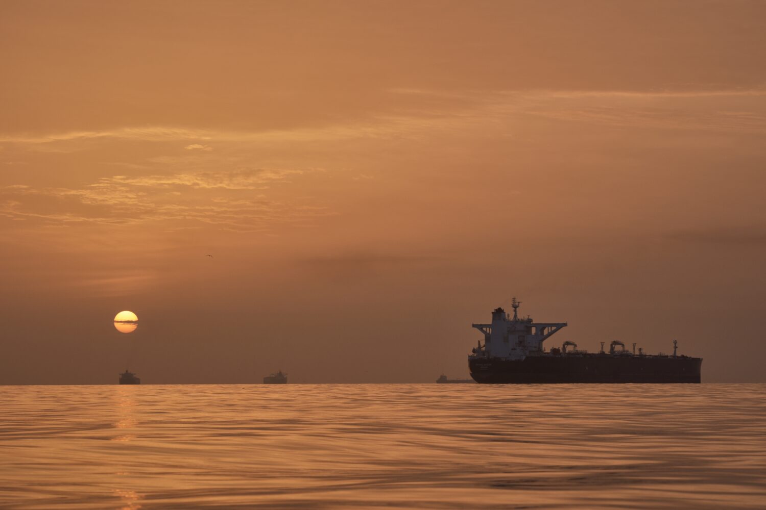 The sun rises behind tankers anchored in the Strait of Hormuz off the coast of Qeshm Island, Iran, ...
