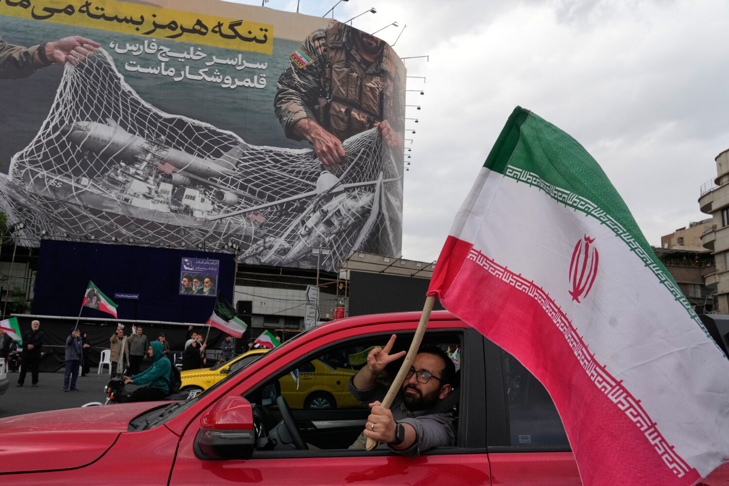 A man flashes a victory sign as he carries an Iranian flag in front of an anti-U.S. billboard depic...