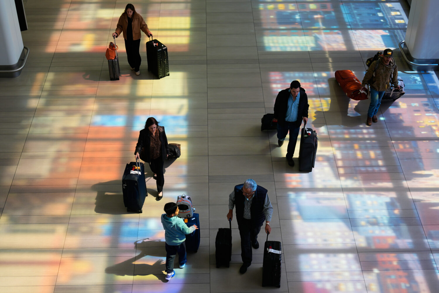 Stained-glass windows cast colorful shadows on the floor as travelers walk through LaGuardia Airpor...