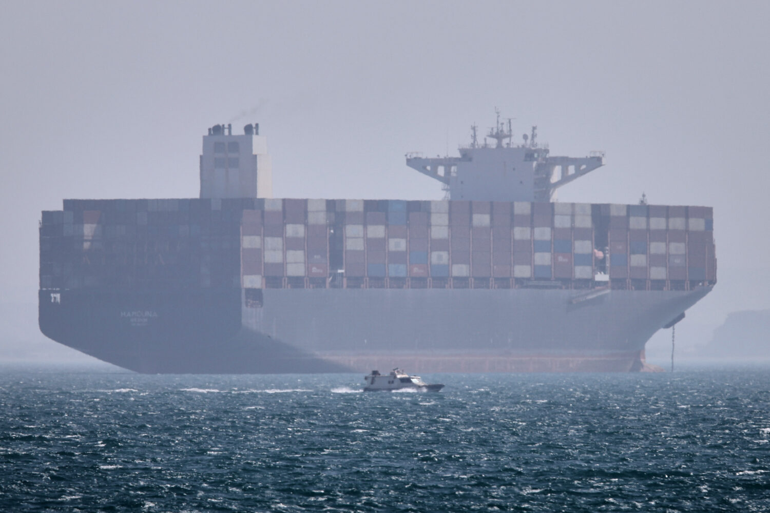 A container ship sits at anchor as a small motorboat passes in the foreground in the Strait of Horm...
