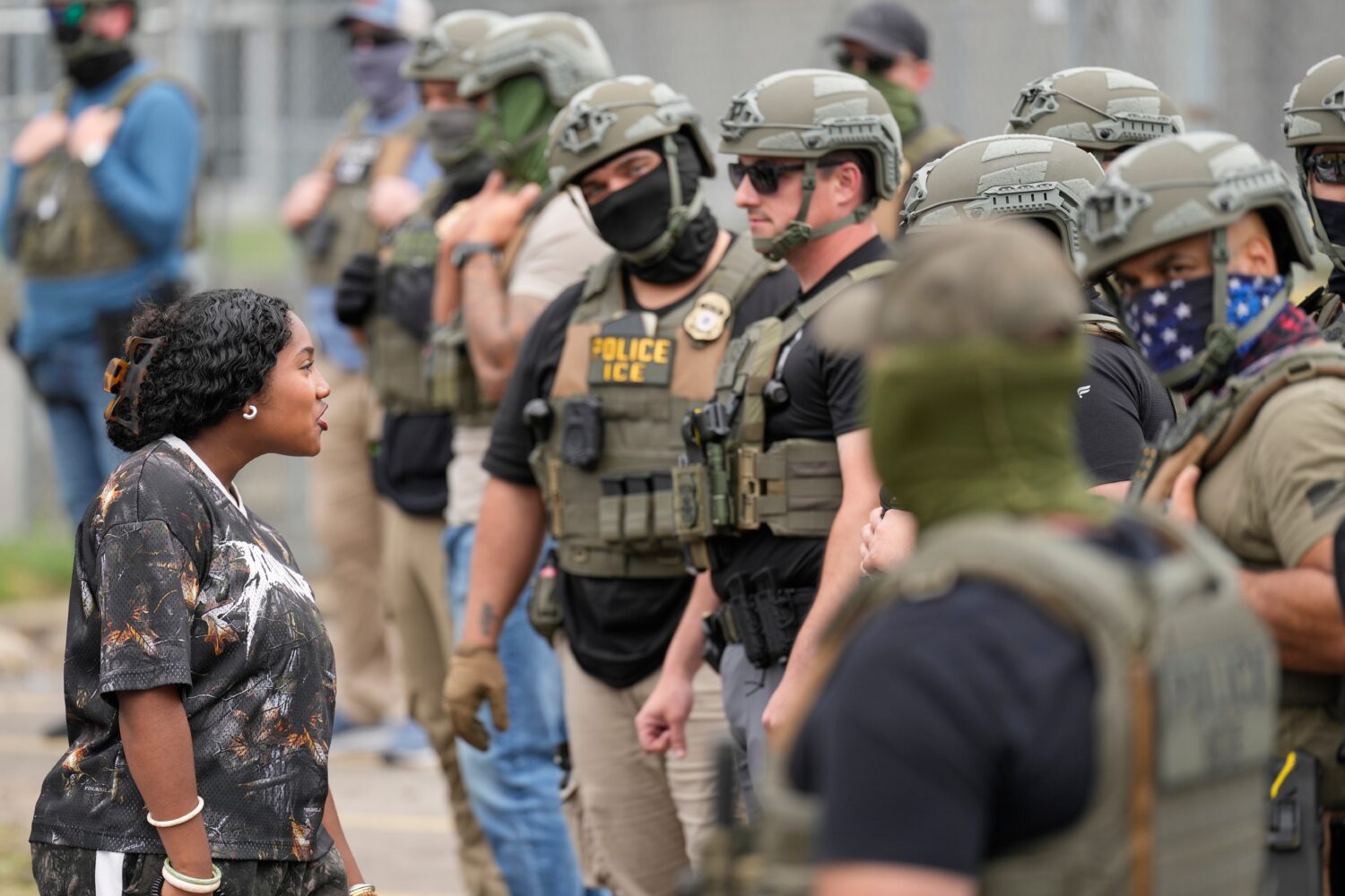 A protester talks to masked federal agents standing outside the Delaney Hall detention center durin...