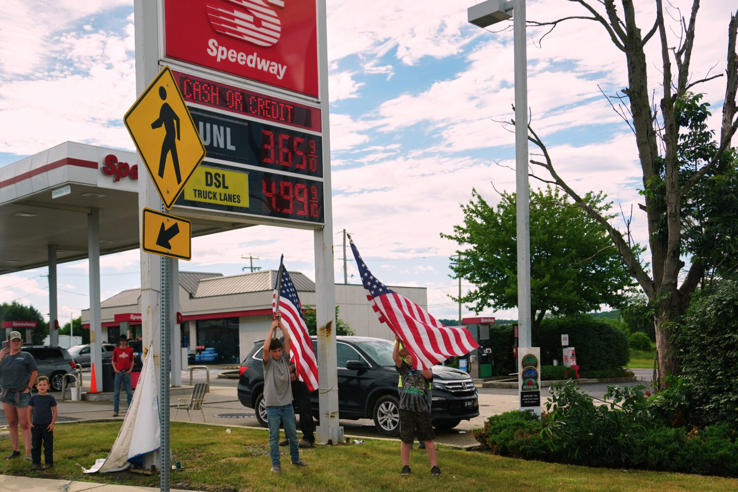 People hold flags in front of a gas station as President Donald Trump's motorcade passes by Tuesday...